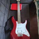 Červená elektrická kytara s bílým pickguardem a světlou hnedou hmatníkem. Na hlavě je viditelné logo "Squier". Kytara má tři snímače a je vybavena če…