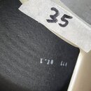 Detailní pohled na část nástroje s krémovým rámem a černým povrchem. Na rámu je nalepený stříbrný štítek s ručně napsaným číslem 35. Na černém povrch…