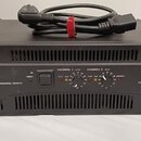 Černý výkonový zesilovač v rackovém provedení s nápisem QSC AUDIO a označením DUAL MONAURAL SUPPLY. Na pravé straně je uveden model RMX 5050 a text P…