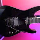Černá elektrická kytara s tvarem těla připomínajícím superstrat. Nástroj má dva humbuckery, přičemž na hradlovém snímači je viditelné logo EMG. Kytar…