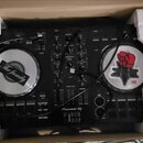 Černý DJ 컨트롤러 v přepravním kartónu s polystyrenovými výplněmi. Na přístroji je vidět bílý nápis Pioneer DJ a menší nápis serato. Oba jog-wheels jsou…