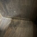 Detail vnitřního rohu dřevěného objektu s tmavým povrchem a viditelnou strukturou dřeva. V levé části je vidět jeden kovový šroub zapuštěný v dřevě.…