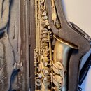 Zlatý saxofon v černém přepravním kufru. Na zvonu je vidět logo s nápisem „SELMER PARIS“ a pod ním menší text „USA“. Nástroj vykazuje mírné známky op…