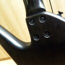 Detail zadní strany černého trupu elektrického nástroje v místě spoje s hnedem. Jsou vidět čtyři šrouby v krku nástroje a jeden ladicí šroubek v horn…