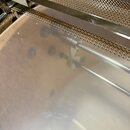 Detailní pohled na kovové části nástroje v stříbrné barvě. Je vidět jemná kovová síťka a hladký, reflexní povrch s několika tmavšími skvrnami. Žádné…