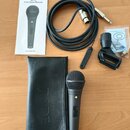 Na fotografii je černý dynamický mikrofon s kovovou síťkou, černý kožený obal s vyraženým nápisem RODE a černý kabel s konektory XLR a 6,35mm jack. S…