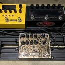 Sada kytarových efektů na černém pedalboardu. V horní řadě jsou žlutý pedál NUX s nápisem DUAL LOOP STEREO, černý přístroj ANAGRAM s logem eff-trade…