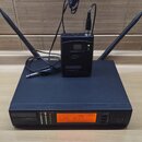 Černý bezdrátový přijímač s dvěma anténami a nápisem LD SYSTEMS WS1000/QR. Na přední straně je oranžový displej s hodnotou 826.300 MHz a řada kontrol…