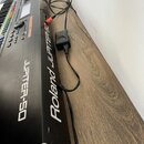 Černý digitální klavír s bílými nápisy Roland JUPITER-50 na bočnici. Nástroj je připojen k elektrické síti pomocí černého síťového adaptéru. Povrch n…