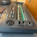 Černý elektronický klavír značky Roland s chybějícími klávesami, v jehož šasi jsou viditelné vnitřní elektronické spoje a desky. Na ovládacím panelu…