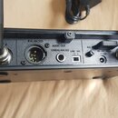 Zadní strana černého elektronického zařízení s dvěma anténami. Jsou zde viditelné nápisy BALANCED, AUDIO OUT UNBALANCED, LINE a MIC. V pravé části je…