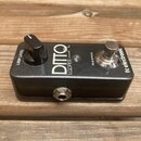 Černý kytarový pedál s nápisy DITTO a LOOPER. Na pravé straně je logo tc electronic a přepínač s nápisem TRUE BYPASS, na levé straně je otočný knoflí…