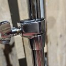 Detail chromovaného kovového stojanu s nastavitelým kloubem a utahovacím šroubem. Povrch vykazuje drobné škrábance a známky opotřebení. Žádné značky…