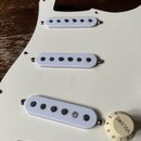 Bílá pickguard s třemi bílými snímači typu single-coil. Na spodním knofíku je nápis VOLUME a stupnice čísel 1 až 10. Povrch je čistý, bez viditelných…