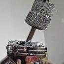 Detailní záběr na kovový mechanismus s nasazeným tlumicím plfeltem šedé barvy. Kovové části mají chromovaný povrch, který vykazuje drobné škrábance a…