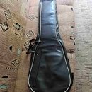 Černý polštovaný pouzdro (gig bag) na kytaru s bílým lemováním po okrajích. Má zipové hlavní oddíly a přední kapsu na příslušenství. Povrch materiálu…