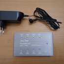 Na fotografii je stříbrný kovový zdroj napájení s nápisy „Harley Benton“, „POWERPLANT ISO-1 PRO“ a „ISOLATED OUTPUT POWER SUPPLY“. Zařízení má osm vý…