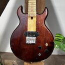 Elektrická kytara s tmavě hnědým trupem z dřeva a světlým hnedým hmatníkem. Nástroj má jeden humbucker v pozici kobylky, stříbrný most s pružinami a…