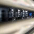 Detailní pohled na čtyři elektronky v řadě, umístěné v černém šasi. Elektronky mají skleněné tělo a jsou zasazeny do černých plastových nebo kovových…