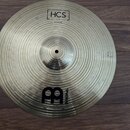 Zlatý cymbál s koncentrickým žebrováním, položený na hnědém laminátovém povrchu. V horní části je nápis HCS, pod ním MADE IN GERMANY a 18" Crash Ride…