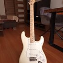 Bílá elektrická kytara typu Stratocaster s bílým pickguardem a javorovým hnedým hmatníkem. Na hlavě nástroje je viditelné logo Squier. Kytara má tři…