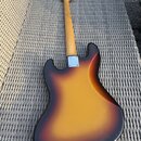 Zadní strana elektrické basové kytary s tělem v barevné kombinaci sunburst. Kytara má dřevěný krk a na spojení krku s tělem je vidět kovový kryt šrou…