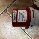 Červený průmyslový elektrický konektor s bílým plastovým krytem. Na červené části jsou dvě nálepky; ta pravá obsahuje nápisy SEZ D.KUBIN, TYP IVN 325…