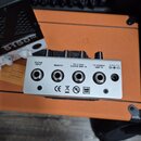 Kovový efektový pedál stříbrné barvy s několika konektory na zadní straně. Nad vstupy jsou nápisy GUITAR INPUT, REMOTE, TO CLEAN GUITAR AMP IN a TO P…