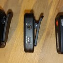 Tři černé plastové přístroje s připevněnou svorkou, položené na dřevěném povrchu. Na dvou z nich jsou viditelné nápisy MIC a USB DC 5V u příslušných…