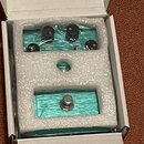 Tyrkysový efekt pedál v bílém polystyrenovém obalu uvnitř kartonové krabice. Na horní části jsou tři černé ovládací knoflíky a nápis REVERB. V dolní…