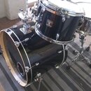 Černá bicí souprava s chromovaným kováním. Na tomu, který je v popředí, je viditelné logo GRETSCH a nápis Blackhawk. Souprava obsahuje basový buben,…