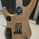Zadní strana elektrické kytary z přírodního dřeva. Na korpusu je kovový štítek s nápisy WASHBURN, VOGGALA a HAND CRAFTED SINCE 1876. V dolní části je…