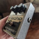 Stříbrný efekt pedál s kovovým povrchem. Na horní části jsou tři černé oválné ovladače s nápisy DELAY a FEEDBACK. Uprostřed je nápis #1 echo a v doln…
