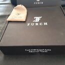 Černá čtvercová krabice s bílým logem FURCH a nápisem Furch CNR System® Active Adjustment Tool Kit na bočním okraji. Vedle krabice je položen béžový…