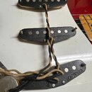 Fotografie zachycuje tři elektrické snímače typu single-coil s černými kryty, které jsou umístěny na bílém pickguardu červené kytary. Na spodním sním…