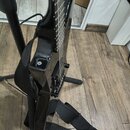 Detailní pohled na černou elektrickou kytaru s lesklým povrchem, která je umístěna na černém stojanu. Nástroj má nasazený černý popruh z textilie. Na…