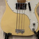 Detail korpusu elektrické basové kytary v krémové barvě s bílým pickguardem. Na snímači je viditelné logo Fender. Nástroj má čtyři struny a chromovan…