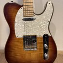 Elektrická kytara s tmelelovým povrchem v hnědém sunburst odstínu a výraznou dřevěnou strukturou. Nástroj má bílý perleťový pickguard a hmatník ze sv…