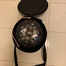 Kovový perkusní nástroj typu steel tongue drum v tmavě modré barvě s geometrickým vzorem na horní straně. Nástroj je umístěn v černém textilním pouzd…