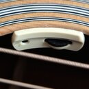 Detailní pohled na bílý plastový prstýnek s černým oválným knoflíkem, který je osazen v otvoru akustické kytary. Prstýnek vykazuje mírné znečištění a…