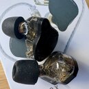 Dva šupenové sluchátka s černými pěnovými nástavci. Mají průhledné plastové tělo a černé kryty. Na sluchátkách nejsou žádné viditelné značky ani nápi…