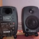 Dva šedé studiové monitory značky GENELEC. Na zadní straně levého reproduktoru je vidět nápis „GENELEC“, modelové označení „8020B BI-AMPLIFIED MONITO…