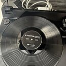Černý turntable s položeným vinylovým diskem. Na štítku disku je bílý nápis TRAKTOR SCRATCH a menší texty, včetně označení MADE IN JAPAN. V horní čás…