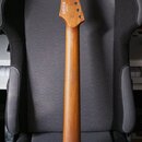 Dřevěný krk elektrické kytary v přirozené hnědé barvě bez hmatníku a pražců. Na hlavě je viditelné logo "Fender" a nápis "Made in USA". Povrch dřeva…