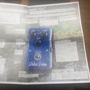 Fotografie zachycuje stránku z uživatelské příručky k efektu Shiba Drive. Na stránce je vidět černý pedál s modrým nápisem Shiba Drive, dvěma ovládac…