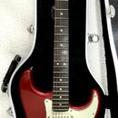 červená elektrická kytara s bílým pickguardem v černém tvrdém kufru. Na hlavě hmatníku je nápis Fender® STRATOCASTER®. Nástroj má tmavý hmatník a tři…