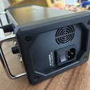 Zadní strana černého elektronického zařízení v kovovém šasi s chromovanou rukojetí. Je zde vidět ventilátor a napájecí konektor s vypínacím tlačítkem…