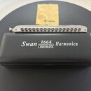 Stříbrná chromatická harmonika s kovovým povrchem a řadou otvorů. Vedle ní je černý plastový obal s bílým nápisem Swan 1664 CHROMATIC Harmonica. V po…