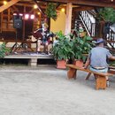 Fotografie zachicuje muzikanta na dřevěném pódiu, který hraje na akustickou kytaru světlé barvy. Vedle něj je umístěn mikrofon na stativu a černý rep…