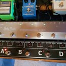 Stříbrný kytarový efektový kontrolér s nápisy Harley Benton a STOMPCONTROL 4 ISO. Zařízení má pět stomečových spínačů, červený digitální displej a řa…